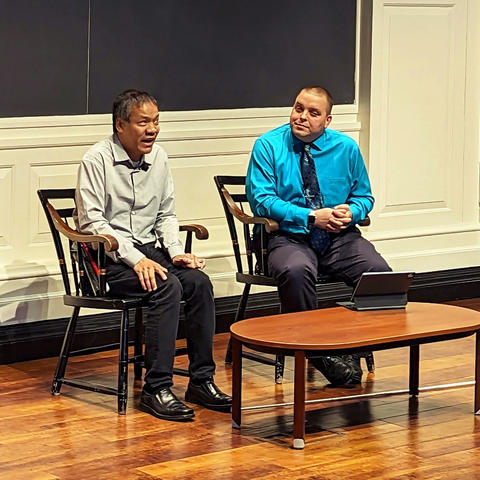 Jennison speaks while Kyle listens, both are seated on stage.